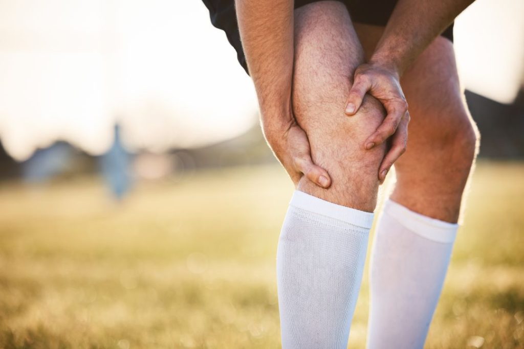 Athlete holding knee in pain on field, seeking chiropractor Auburn, AL for relief and recovery.