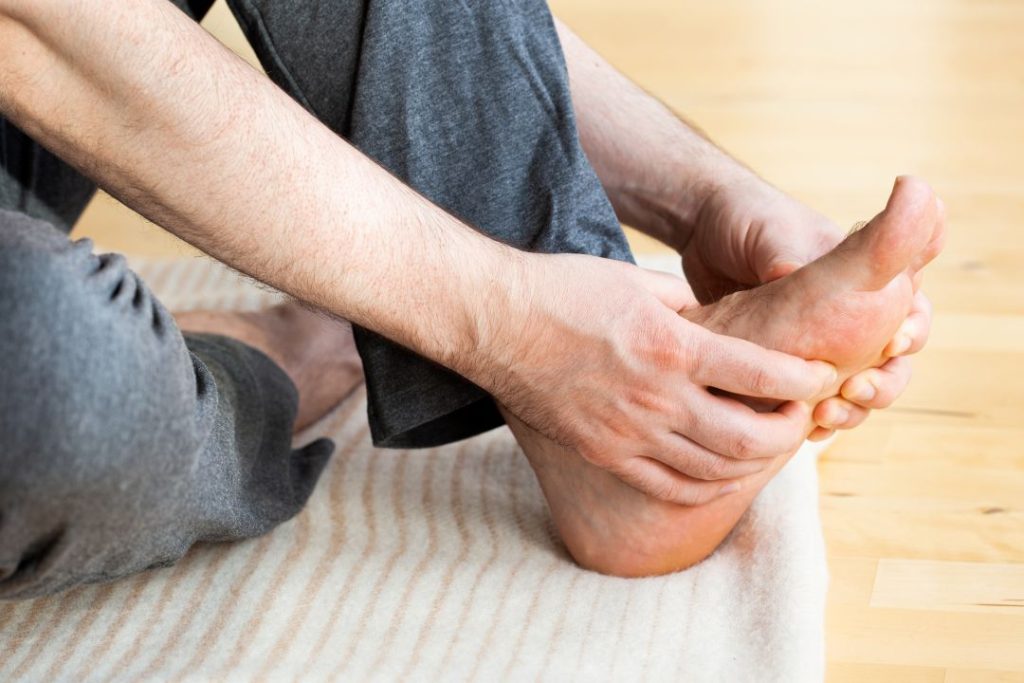 Person massaging foot for pain relief, seeking chiropractor Opelika, AL services.