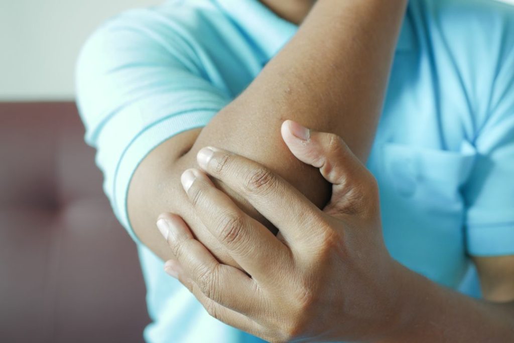 Person holding elbow in pain, seeking relief from chiropractor Auburn, AL.