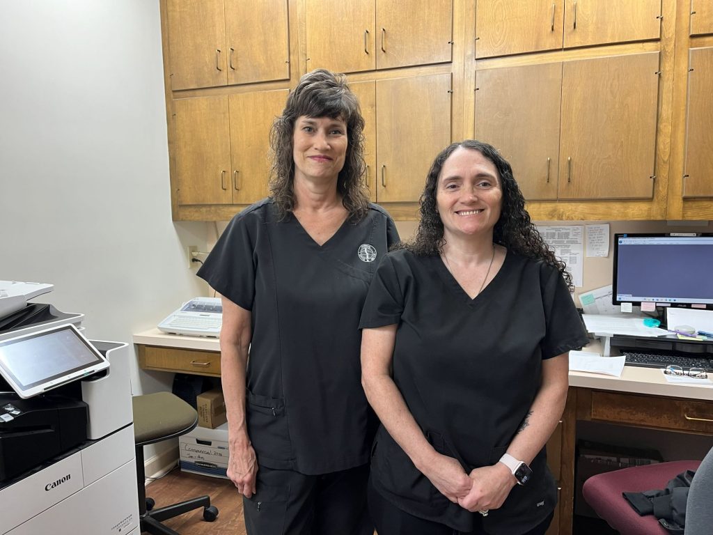 Chiropractor team in Opelika, AL office, standing smiling in uniforms, ready to assist patients.