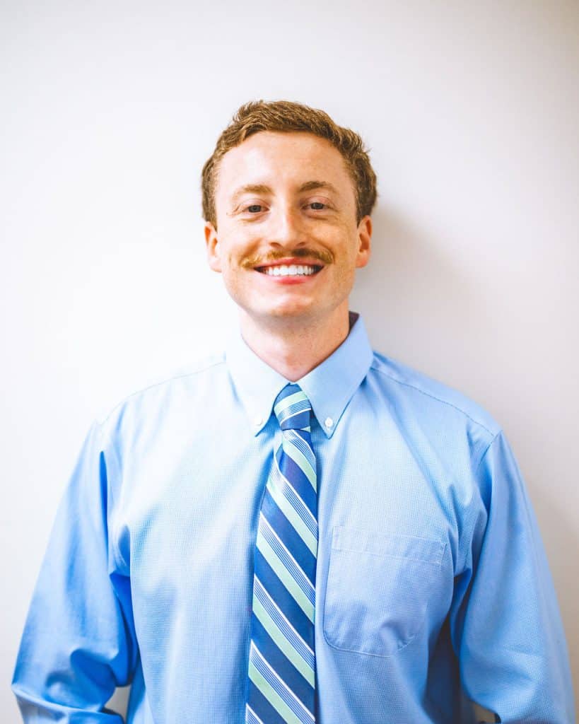 Friendly chiropractor in Auburn, AL, in blue shirt with striped tie, smiling against a neutral background.