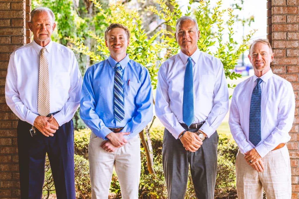 Team of professionals ready to assist at a chiropractor in Opelika, AL, standing outdoors in dress shirts and ties.