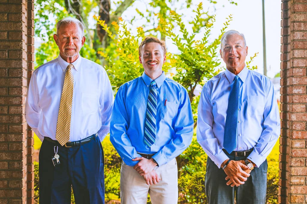 Three professionals in ties smiling outside. Chiropractic specialists in Opelika, AL enhancing well-being.