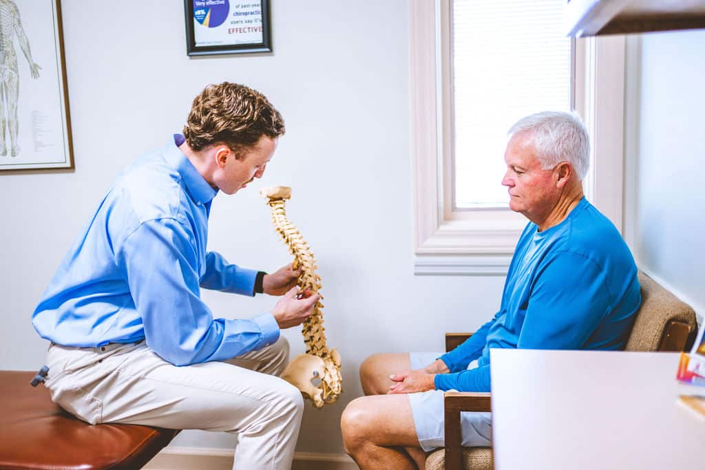 Chiropractor in Opelika, AL explaining spinal health with a model to a patient in a clinic setting.